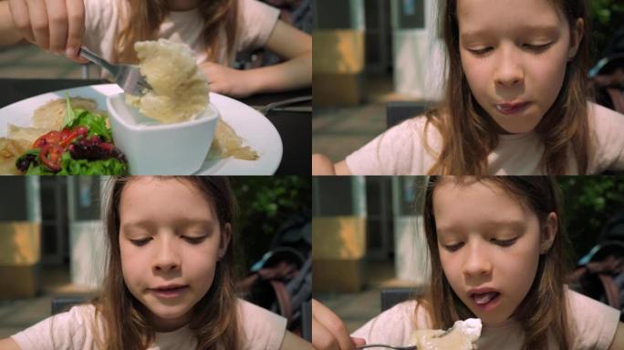 小女孩贪婪地吃美味的土豆饺子，用叉子蘸上土豆饺子，在餐馆的肖像视图中