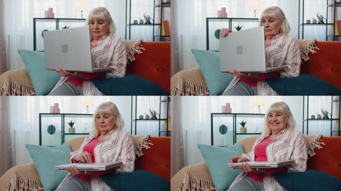高级祖母妇女使用笔记本电脑，在家里的房间里打字，看着相机，微笑着