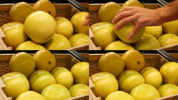 交易篮子中许多美丽的柚子的特写镜头，男性买家的手拿了一个