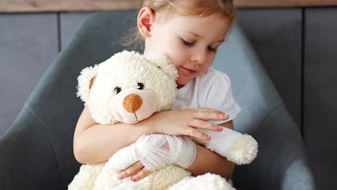 在医院的医生预约时，手指折断的小女孩抱着用绷带包扎的爪子的泰迪熊