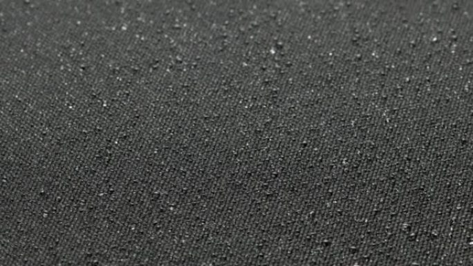 水滴覆盖的黑色疏水织物的纺纱特写背景