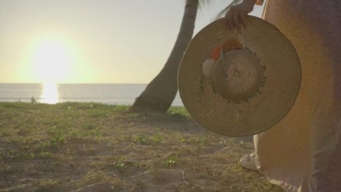 女人拿着太阳帽走在海滩上。假期日落背景。夏威夷。