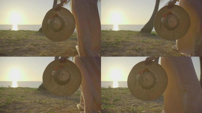 女人拿着太阳帽走在海滩上。假期日落背景。夏威夷。