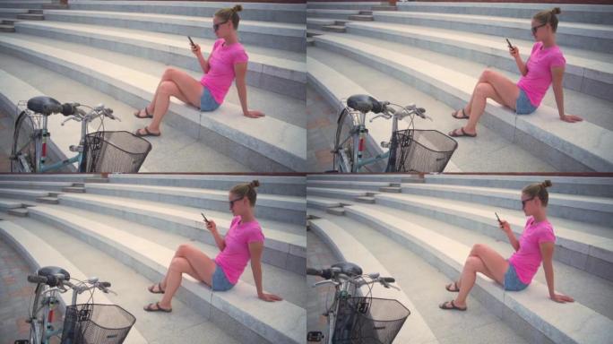 带智能手机的女孩坐在楼梯上，骑自行车日落快速慢动作