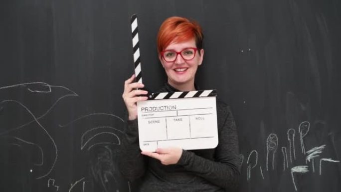 红发女女演员与电影拍板合影，微笑着看着黑板背景下的相机。