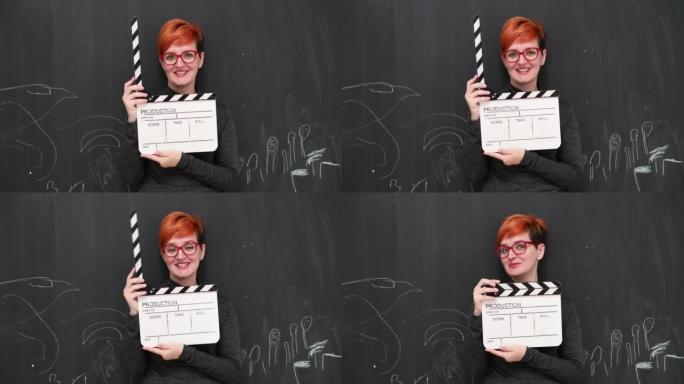 红发女女演员与电影拍板合影，微笑着看着黑板背景下的相机。