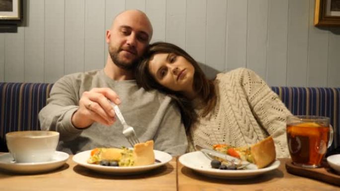 餐馆里的年轻夫妇喝茶吃食物有趣地用素食蛋糕片互相喂养，心情愉快
