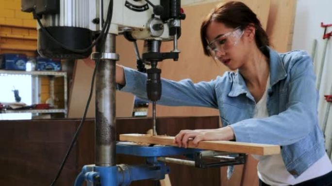亚洲木工女工用钻床在木工车间工厂钻木