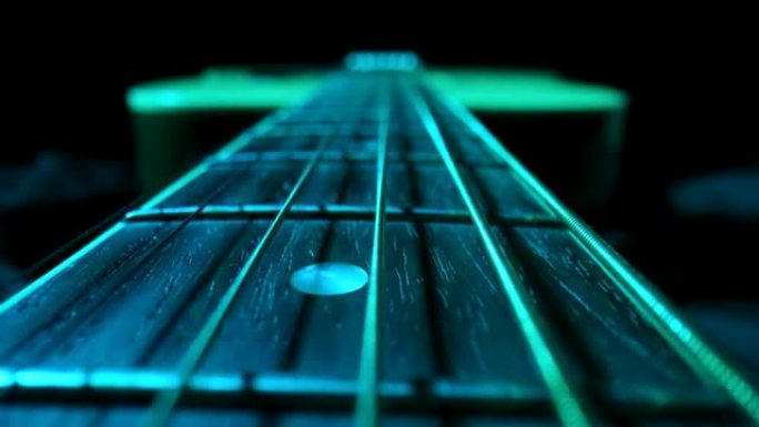 黑色背景下的古典原声吉他指板，被蓝光照亮。棕色木制吉他琴颈，配有金属琴弦和琴弦。弦乐器