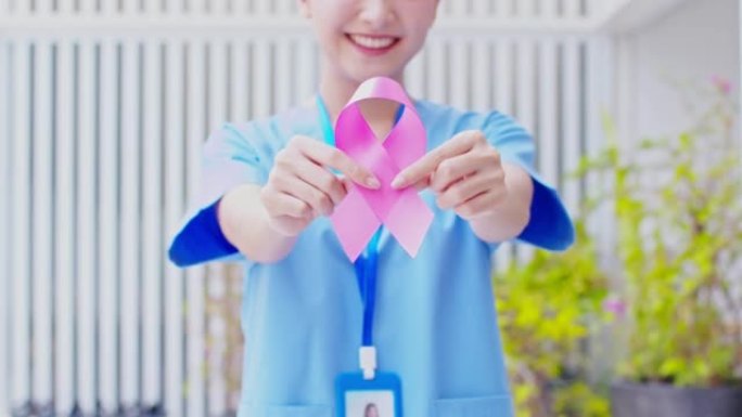 手持粉红丝带的亚洲医生微笑积极的情感，支持人们治愈和抗击乳腺癌。10月乳腺癌宣传月。医疗保健和保险概