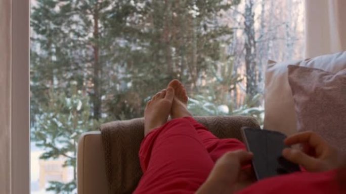 一个穿着红色衣服的女孩躺在沙发上，俯瞰着被雪覆盖的后院。一个年轻的女人没有注意到她周围的美丽，埋在她