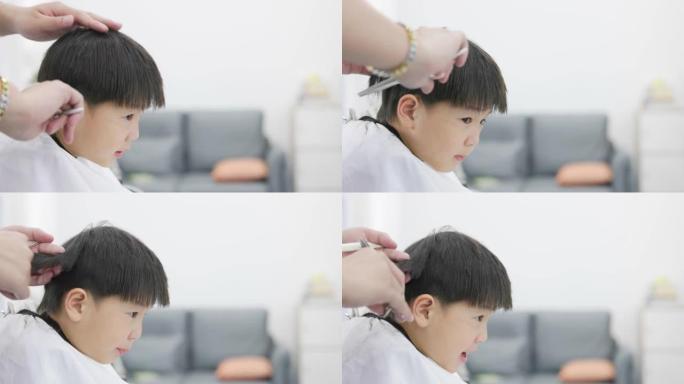 小男孩坐在理发店的椅子上被理发师理发