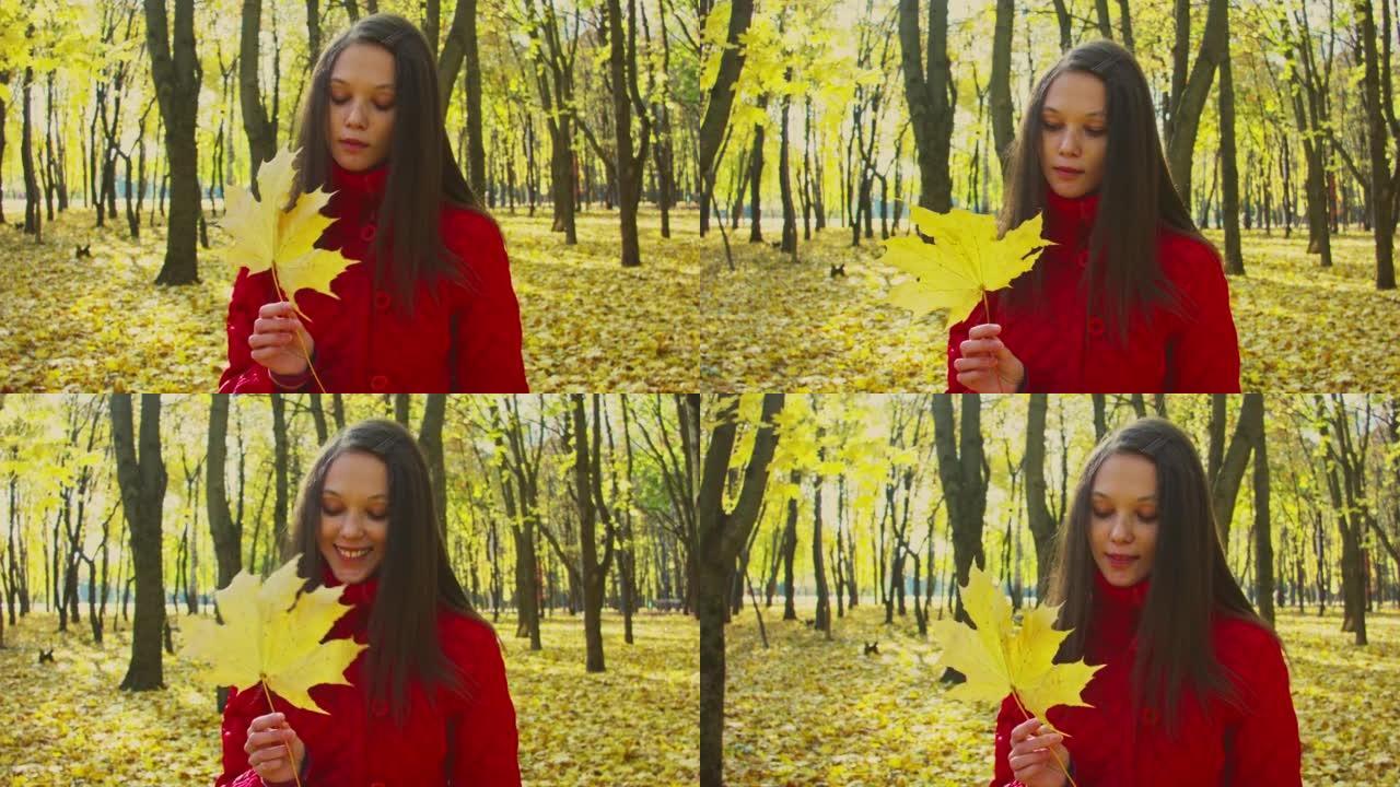 日落时，一个年轻女子拿着枫叶站在森林里的特写镜头。