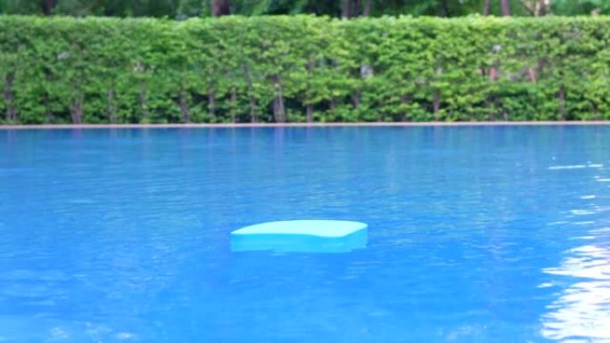 蓝色的游泳板或踢脚板漂浮在游泳池的水面上，游泳池边的夏季度假娱乐活动对象