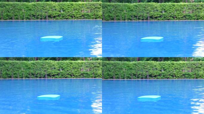 蓝色的游泳板或踢脚板漂浮在游泳池的水面上，游泳池边的夏季度假娱乐活动对象