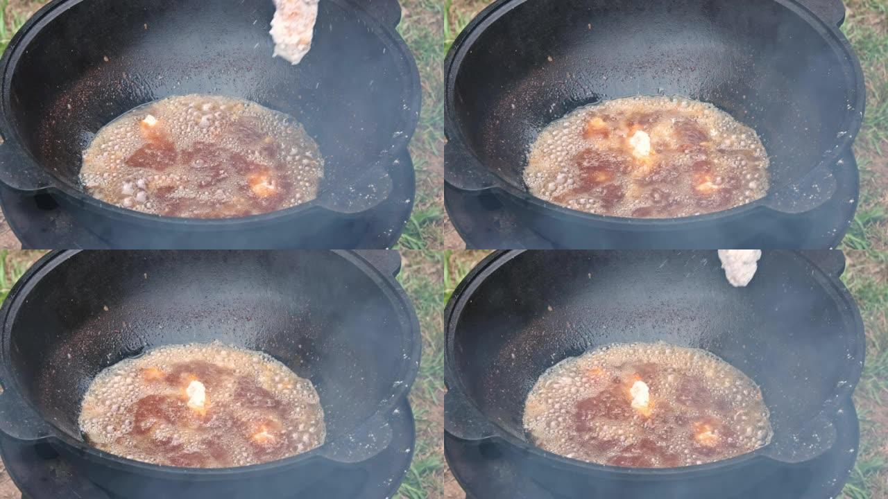 厨师正在在木头上的大锅中煎炸鸡翅，油正在沸腾