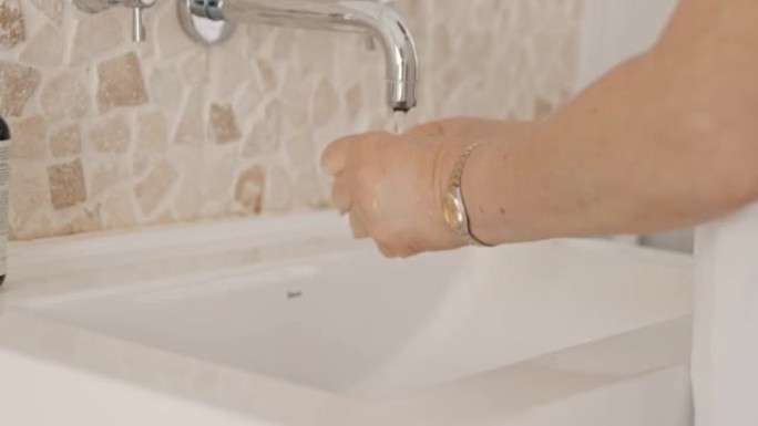 不知名的高级妇女在家里的水槽里洗手。不知名的老年妇女使用浴室水槽洗手，清洁，身体护理