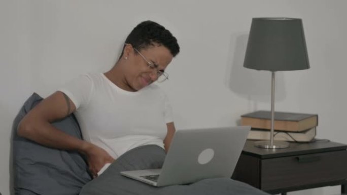 非洲妇女在床上使用笔记本电脑时背部疼痛