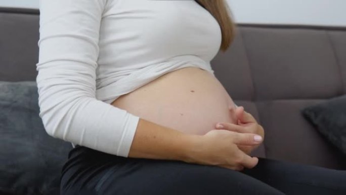 一位皮肤白皙的孕妇坐在舒适的沙发上抚摸着她的肚子