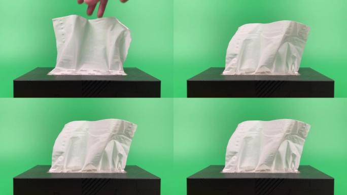 慢动作，一个人的手从隔离在绿色背景上的纸巾纸盒中拉出一块纸巾。