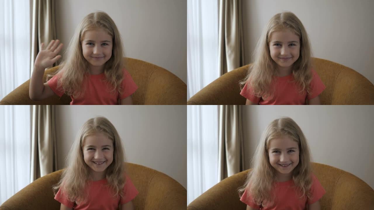 肖像有趣的女孩微笑着看着相机。快乐可爱的小视频记录器打你好，看着摄像头和网络摄像头说话。坐在沙发上进