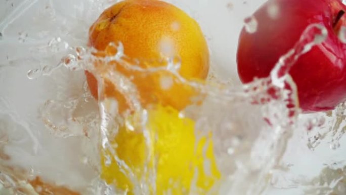 将橙子，柠檬和苹果倒入玻璃碗水中。慢动作。