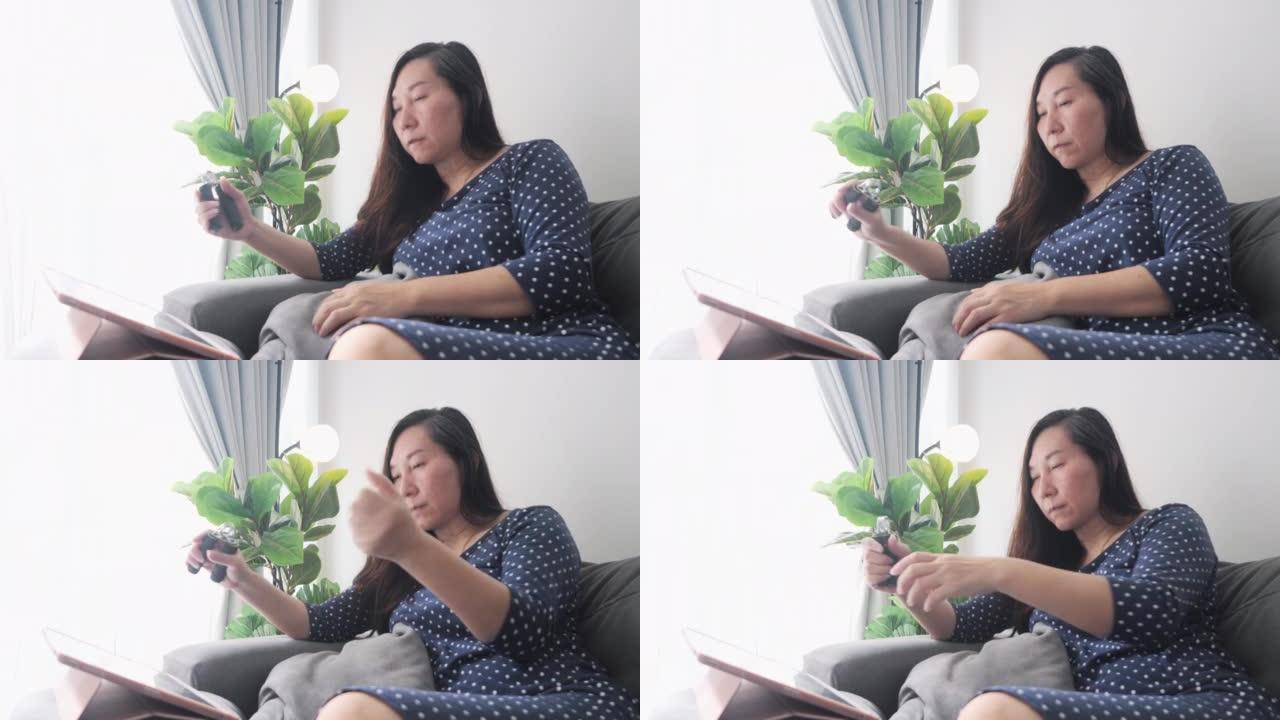 亚洲成年女性坐在沙发上，看着如何用数字平板电脑按摩手，遵循健康的生活方式理念。
