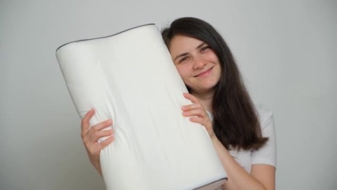 一名妇女抱着她最喜欢的矫形白色枕头，看着镜头微笑