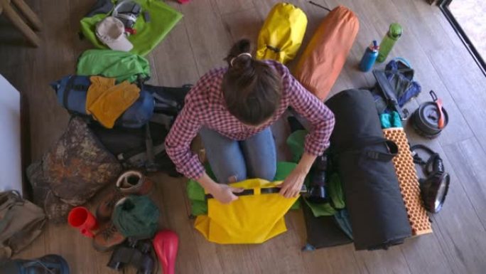 西班牙裔年轻女子打包露营和徒步旅行设备准备打包旅行的慢动作平移视图