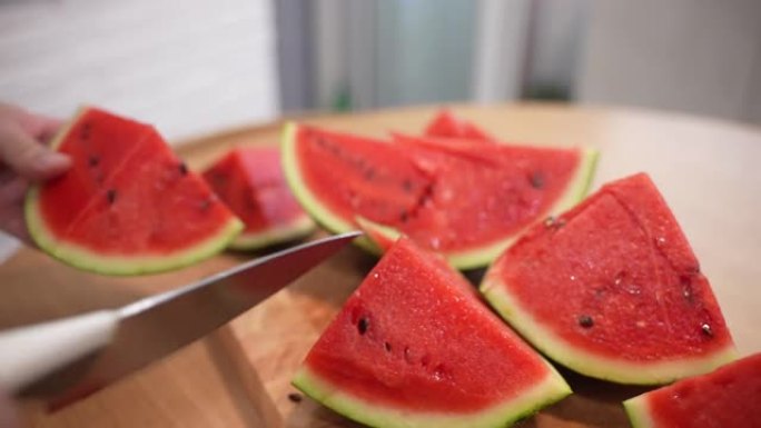 多汁的成熟西瓜在木板上切成小块，人用菜刀将夏季水果切成小块，开胃的红色西瓜，里面有黑色种子，水果收获