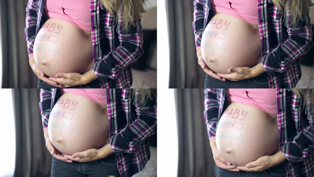 孕妇抚摸着她怀孕的肚子，温柔，爱与爱，粉红色和蓝色的婴儿加载铭文画在女人的肚子上，等待婴儿到来的女人