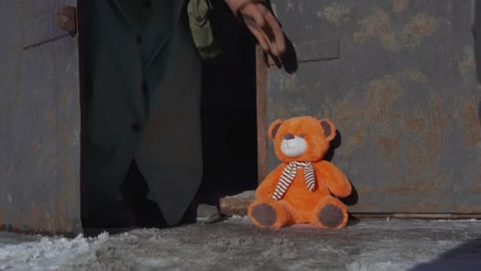 身穿防核服、戴着手套的士兵举起被遗弃的玩具熊