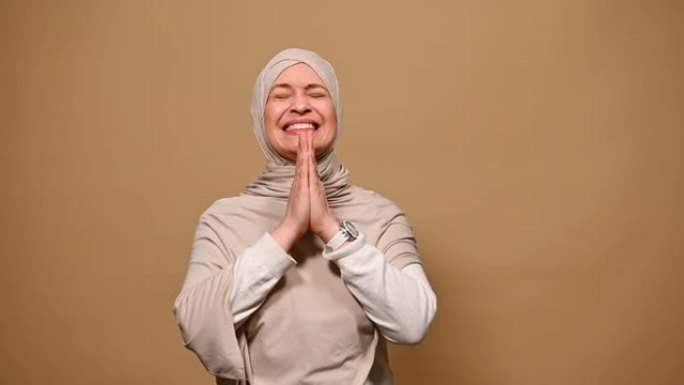 穆斯林妇女戴着米色头巾，交叉手指，许下美好的愿望，希望她的梦想成真