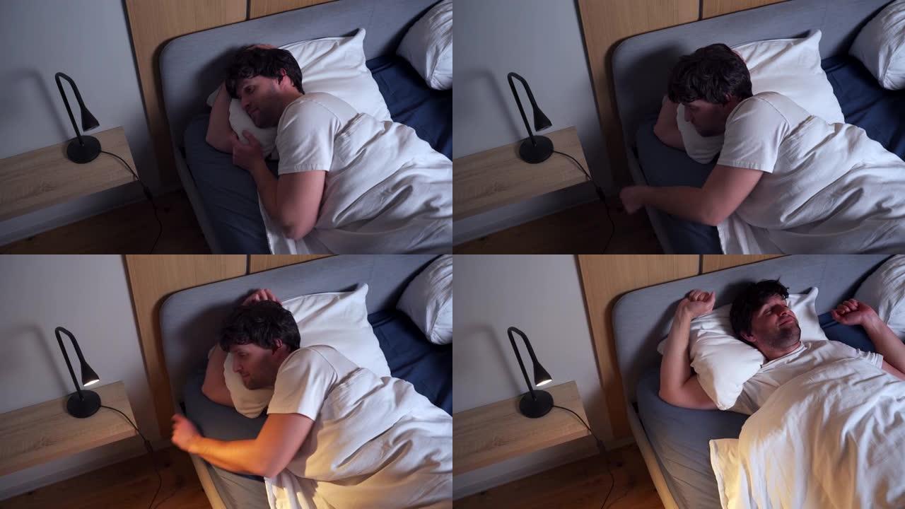 年轻的黑发男人打开灯醒来，伸展身体，躺在卧室的床上一个满意的男人在床上放松