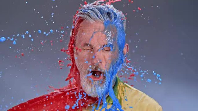 SLO MO LD大胡子的男人被红色和蓝色的油漆打中时感到惊讶
