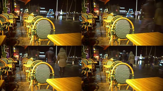 空荡荡的街头餐厅的桌椅，人们走过，雨夜
