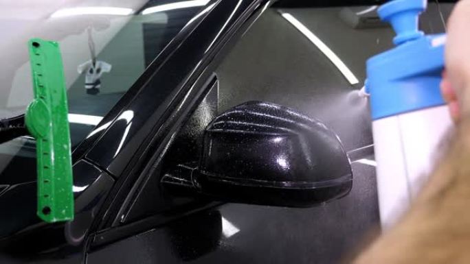 汽车修理工在车身上喷水。保护膜的胶合。