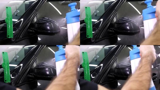 汽车修理工在车身上喷水。保护膜的胶合。
