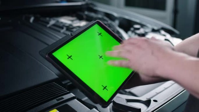 一位不知名的男性汽车服务人员站在打开的引擎盖附近，用绿色屏幕的数码平板电脑检查汽车并进行维护