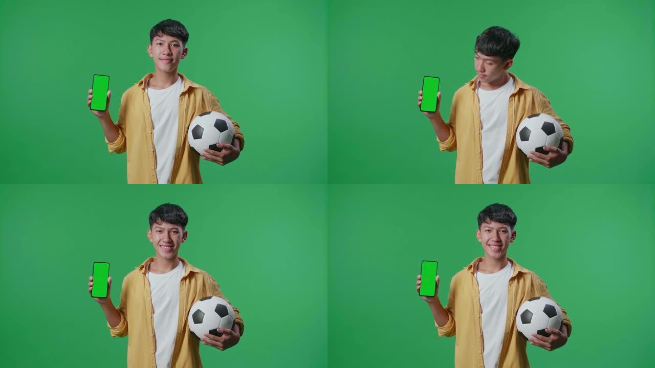 亚洲男孩的球显示模拟绿屏智能手机，并在绿屏背景上欢呼足球时摇摇头
