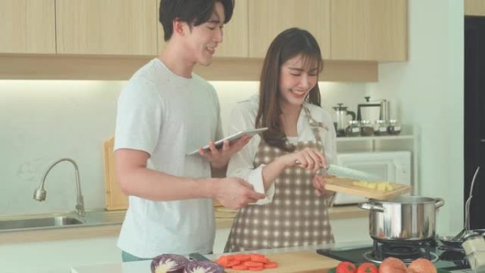 亚洲夫妇在数字平板电脑上寻找食谱，在他们的家庭厨房里做鸡汤。一对情侣的浪漫场景