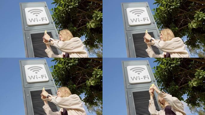 年轻女孩正试图在城市公园的wifi标志旁边获得wifi。这个女孩拿起电话，用互联网在斯特拉旁边捕捉网