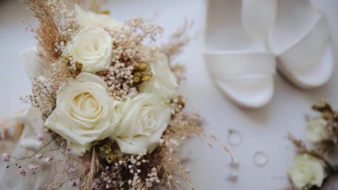 以波西米亚风格的婚礼装饰的桌子上的特写美丽的玫瑰和干花花束。桌子上订婚的模糊鞋子和戒指
