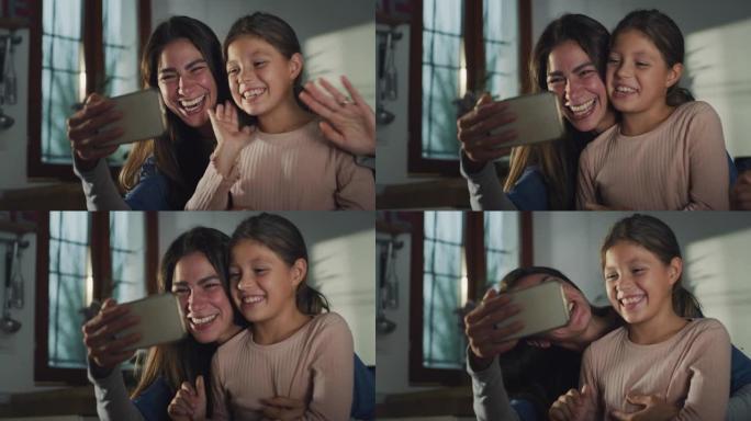 小女孩与母亲一起使用智能手机与家人坐在厨房里与家人进行视频通话的真实照片。女人和她的女儿挥舞着问候，