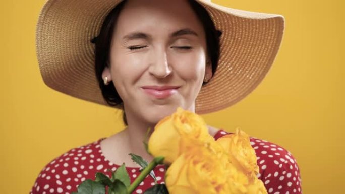 女人眨眼。快乐微笑的女人，手里拿着一束鲜花，黄色背景眨眨眼看着相机。爆头