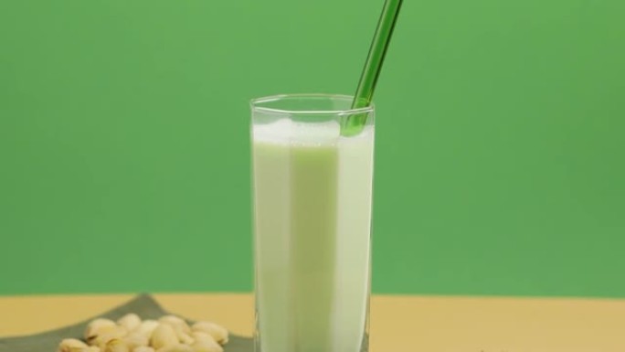 开心果牛奶在玻璃和开心果的米色绿色背景下，相机向下倾斜。无乳糖开心果牛奶和散开心果