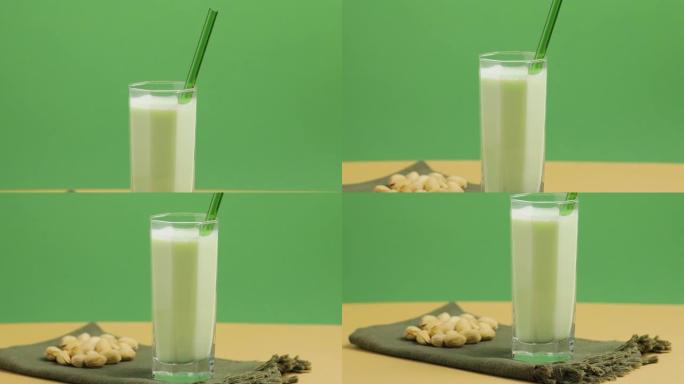 开心果牛奶在玻璃和开心果的米色绿色背景下，相机向下倾斜。无乳糖开心果牛奶和散开心果