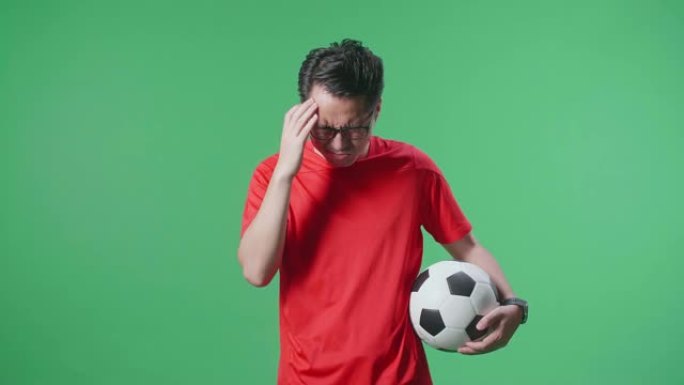 亚洲男子带球正在为射门而生根，并在绿屏背景上欢呼足球时后悔
