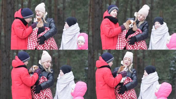 母亲和三个孩子的幸福家庭的视频裹着毯子，抱着并亲吻骑士查尔斯·金狗，在冬季森林散步。冬季露营和寒冷的