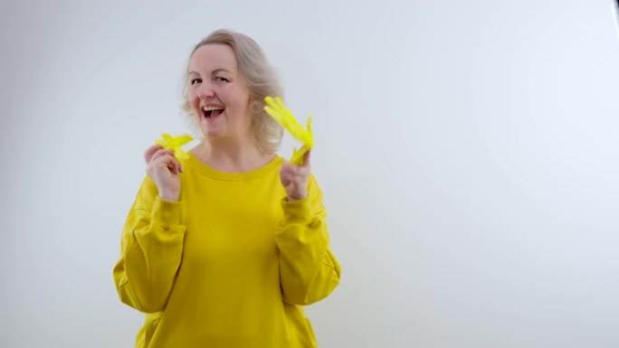 挥舞着乳胶手套的女人将黄色乳胶手套戴在手上美丽，性感的女人，家庭主妇，穿着白色毛衣和黄色手套